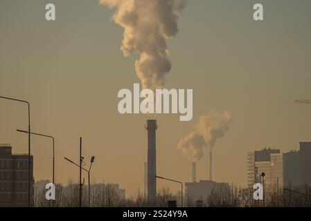 Rauch aus Industrieschornsteinen vor Sonnenuntergang, der die Umweltauswirkungen der Industrie auf städtische Landschaften unterstreicht Stockfoto