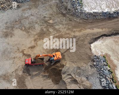 Luftaufnahme eines Baggers, der Sand in einen Lkw lädt, Draufsicht. Schießen von einer Drohne aus. Erdbewegungsgeräte. Stockfoto