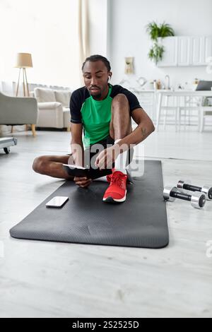 Ein junger afroamerikanischer Mann arbeitet ferngesteuert auf einer Yogamatte, um Fitness und Produktivität auszugleichen. Stockfoto