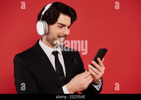 Ein stilvoller junger Mann mit dunklem Haar hört Musik und setzt sich mit seinem Smartphone auseinander und strahlt Charme aus. Stockfoto