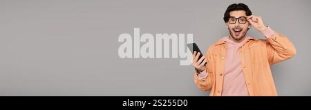 Ein junger Mann mit Brille zeigt sein Smartphone in einem eleganten, modernen Interieur. Stockfoto