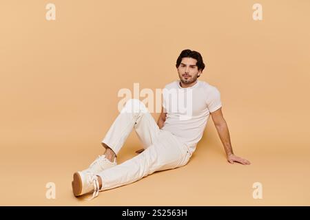 Ein junger Mann mit brünetten Haaren entspannt sich vor einem warmen gelben Hintergrund in lässigem Stil. Stockfoto