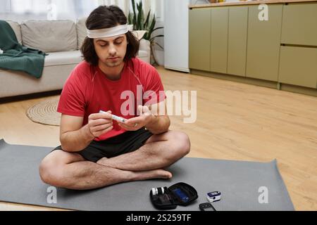 Ein junger Mann übt sich zu Hause selbst aus und überprüft seinen Blutzuckerspiegel, während er bequem sitzt. Stockfoto