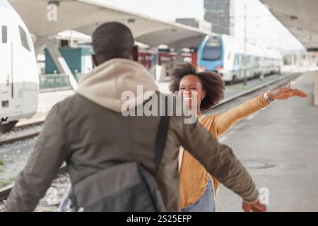 Afroamerikanisches Paar trifft sich an einem Bahnhof in der Nähe des angekommenen Zuges und drückt die Begeisterung für ihre bevorstehende gemeinsame Reise aus. Stockfoto