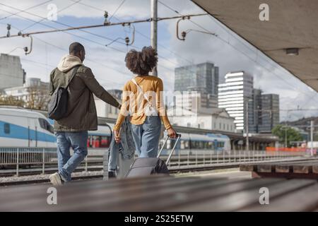 Afroamerikanisches Paar, das Koffer entlang eines Bahnhofs trägt, bereit für die Zugfahrt. Lebensstil-Konzept für Reisende. Stockfoto