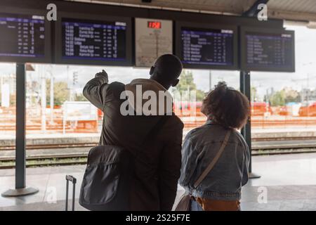Afroamerikanisches Paar überprüft den Fahrplan Ankunft Abfahrtskarte an einem Bahnhof. Informations-, Transport- und Tourismuskonzepte. Stockfoto