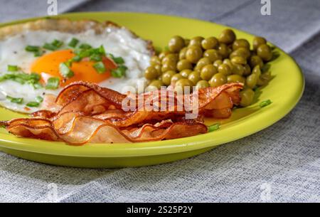 Rührei mit Speck und grünen Erbsen auf einem Teller, Blick von oben. Stockfoto
