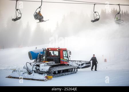 Großer Schnee-Reinigungsmaschine arbeitet an Skipiste unter Kabel Stühle Stockfoto