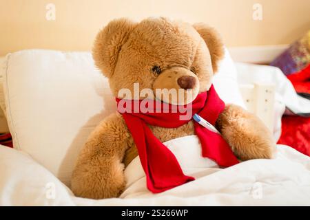 Nahaufnahme Foto der braune Teddybär in Lesen Sie Schal im Bett liegend, mit thermometer Stockfoto