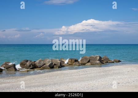 Ruhiges türkisfarbenes Wasser des Tyrrhenischen (mediterranen) Meeres. Künstliche und natürliche Wellenbrecher. Horizont des Wassers und des Sandstrandes. Blauer Himmel mit weiß Stockfoto