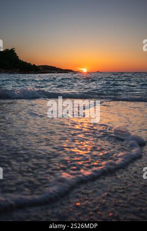Romantischer vertikaler Blick auf die Ionische Meereswelle mit Sonnenuntergang in Ksamil. Niedriger Wasserwinkel während der Goldenen Stunde mit Orange Sun an der albanischen Riviera. Stockfoto