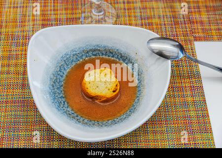 Aus nächster Nähe sehen Sie Tomatensuppe mit goldgerösteter Brotscheibe, serviert in einer weißen Schüssel auf farbenfroher gewebter Tischdecke. Stockfoto