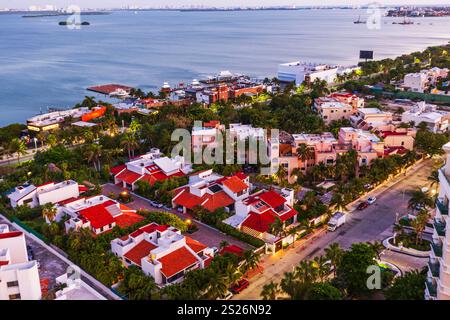 Blick aus der Vogelperspektive auf die karibische Küstengegend in der Dämmerung mit roten Häusern, umgeben von Palmen und ruhigem Meer. Mexiko. Cancun. Stockfoto