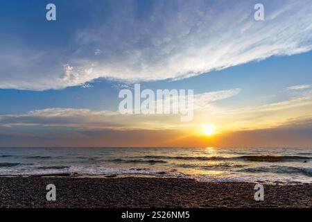 Ein atemberaubender Sonnenuntergang über dem Meer, mit einem atemberaubenden Himmel voller lebendiger Farben und flauschiger Wolken. Stockfoto