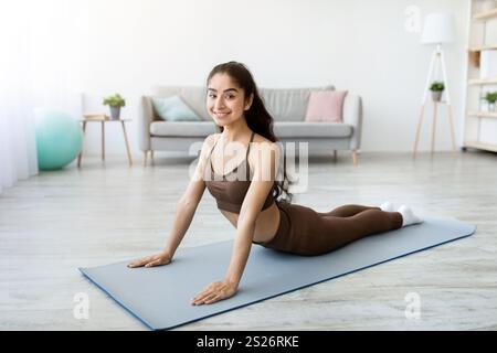 Eine fitte junge Indianerin, die Yoga praktiziert, Kobra zu Hause macht, in voller Länge Stockfoto
