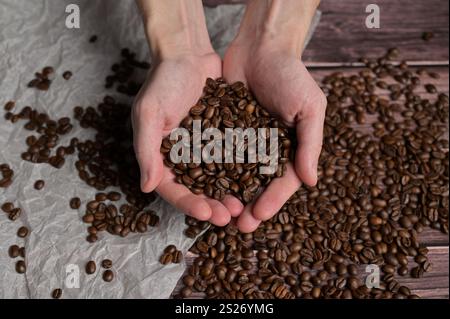 Die Hände des Mannes, die frisch aromatisch geröstete Kaffeebohnen halten. Arabica- und Robusta-Mischung. Holztisch und Hintergrund aus Bastelpapier Stockfoto