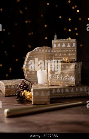 Wunderschön gewickelte Weihnachtsgeschenke mit braunem Papier und goldenen Bändern, umgeben von weichem Kerzenlicht und natürlichen Tannenzapfen, die Wärme und festliche Atmosphäre wecken Stockfoto