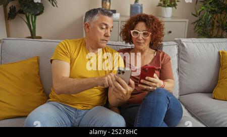 Paare mittleren Alters sitzen zusammen auf einem Wohnzimmer Sofa, während sie Smartphones benutzen, und zeigen Liebe und Gesellschaft in einem gemütlichen Wohnraum Stockfoto