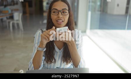 Junge Frau, die in einem Büro in der Nähe eines Fensters in einem Smartphone spricht. Stockfoto