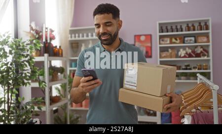 Junger hispanischer Mann, der in einem Wohnkultur-Laden einkaufen und Pakete hält und sein Handy in einem stilvoll dekorierten Innenraum ansieht Stockfoto
