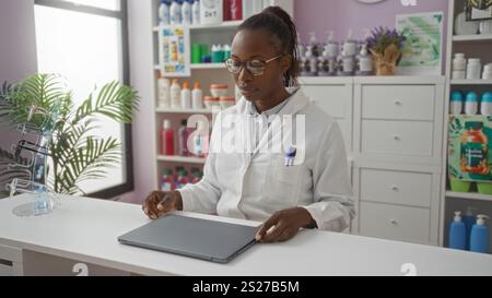 Apothekerin in einer Apotheke, die in einem modernen, gut sortierten Drogeriemarkt mit weißem Labormantel und Brille einen Laptop öffnet Stockfoto
