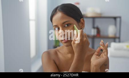 Junge Frau mit brünetten Haaren mit Hautpflegewerkzeug im Spa-Salon mit Wellness-Inneneinrichtung, Schwerpunkt auf Schönheitsbehandlungen. Stockfoto