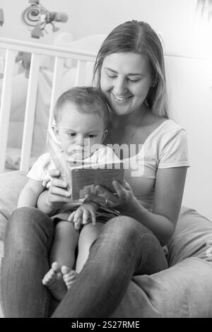 Schwarz-weiß-Porträt der jungen Mutter, die mit Baby im Sitzsack sitzt und Buch liest Stockfoto