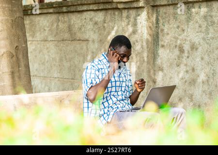 Junger, fröhlicher schwarzer Mann, der Handy und Laptop benutzt. Moderner Lifestyle Stockfoto
