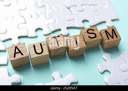 Wort Autismus gemacht mit Holzwürfeln und Puzzleteilen auf hellblauem Hintergrund, Nahaufnahme Stockfoto
