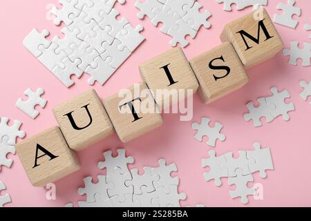 Wort Autismus gemacht mit Holzwürfeln und Puzzleteilen auf rosa Hintergrund, flach gelegt Stockfoto