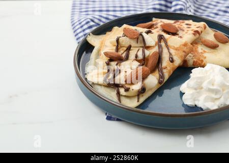 Köstliche Crepes mit Schokoladensoße, Mandeln und Schlagsahne auf weißem Tisch, Nahaufnahme Stockfoto