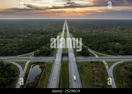 Erhöhter Blick auf die Autobahnabzweigung über Fahrspuren mit schnell fahrenden Autos und Lkws bei Sonnenaufgang. Verkehrsinfrastruktur auf der Interstate Stockfoto