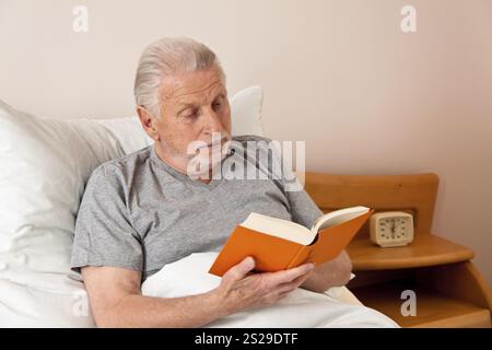 Eine Seniorin in einem Altersheim liest ein Buch im Bett Osterreich Stockfoto