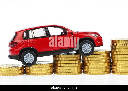 Ein Modellauto und Münzen vor weißem Hintergrund, symbolisches Foto für Preiserhöhungen, Benzinkosten und Autokosten. Österreich Stockfoto