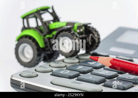 Ein Traktor und ein roter Stift auf einem Rechner. Kosten für Benzin, Verschleiß und Versicherung. Kosten und Subventionen in der Landwirtschaft Osterreich Stockfoto