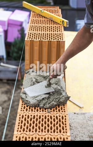 Anonymer Bauarbeiter auf einer Baustelle, der eine Mauer errichtet. Ziegelmauer eines soliden Hauses. Symbolisches Image für illegale Arbeit und Bungling Stockfoto