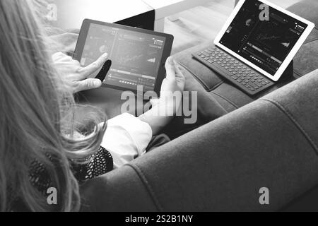 Brünette Frau mit digitalen Talet und Laptop-Computer auf Sofa im Wohnzimmer, schwarz / weiß Stockfoto