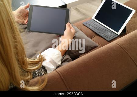 Brünette Frau mit digitalen Talet und Laptop-Computer auf Sofa im Wohnzimmer Stockfoto