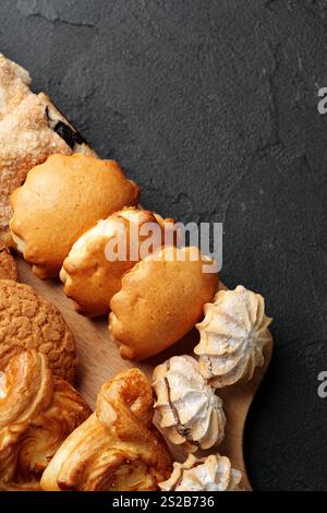 Frisch gebackene Auswahl an köstlichen Keksen und Gebäck auf einer Holzplatte mit dunklem strukturiertem Hintergrund Stockfoto