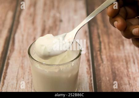 Dieses Bild zeigt eine Nahaufnahme einer Hand, die einen Löffel mit weißem, cremigem Joghurt hält. Stockfoto