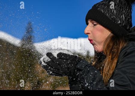 Eine junge Frau, die Schnee aus ihren Händen bläst und eine Menge Schneeflocken in einem Winterwunderland erzeugt. Stockfoto