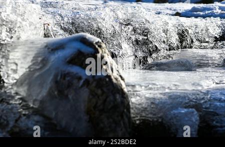 Eiszapfen hängen an Felsen, während gefrorenes Wasser über sie fließt, was eine wunderschöne Winterszene schafft. Stockfoto