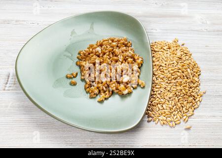 Ganze Dinkelkörner und gekochter Brei auf grünem Teller Holztisch Stockfoto