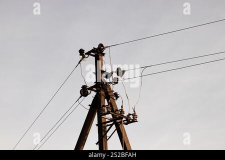 Nahaufnahme des oberen Teils eines elektrischen Posts mit Stromleitungen, die sich über den Himmel erstrecken Stockfoto