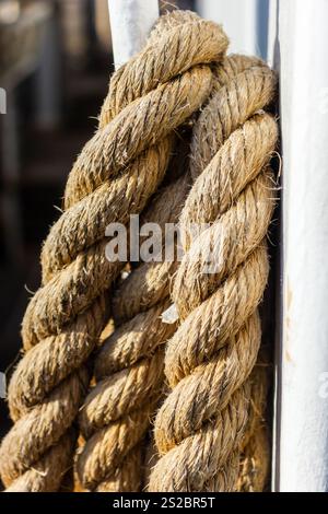 Eine detaillierte Nahaufnahme eines dicken, strukturierten Faserseils, das sicher um einen Metallmast im Außenbereich gebunden ist, unterstreicht das robuste Erscheinungsbild und Stockfoto