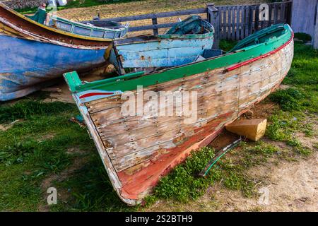 Eine Szene mit alten Holzbooten, verwittert von der Zeit, auf grasbewachsenem Land in der Nähe eines Zauns, die eine rustikale und ruhige maritime Atmosphäre vermitteln. Stockfoto