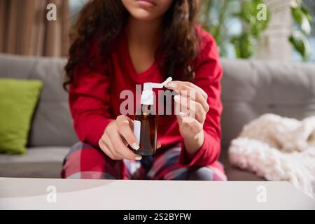 Zugeschnittenes Foto von Frau passt die Sprühdüse auf braune Glasflasche an, die auf der Couch im Wohnzimmer sitzt. Stockfoto