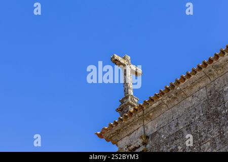 Religiöses christentum-Kreuz aus Granit auf dem Dach einer Kirche mit blauem Himmel in Quintela Portugal. Stockfoto