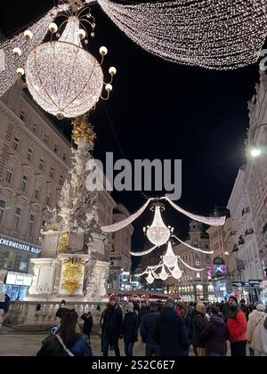 Weihnachtsbeleuchtung in der Fußgängerzone in der Nähe des Stephansplatzes mit dem Denkmal für die Pest-Säule. Die Lichter sind elegante Kronleuchter, die über der Straße hängen. Stockfoto