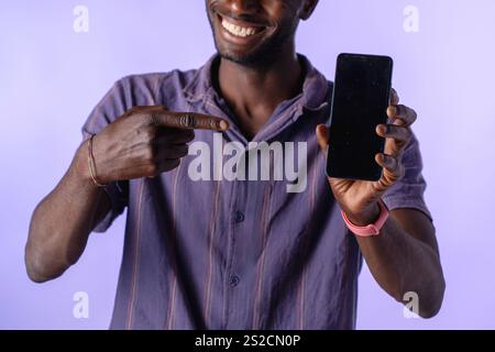 Isolierter afrikanischer Mann, der lächelnd auf ein Smartphone zeigt, mit leerem Bildschirm für Mockup-Zwecke Stockfoto